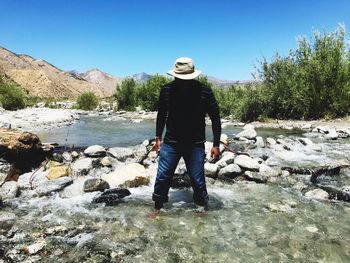 Rear view of man standing on rock by river against clear sky