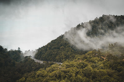 Clouds storm in between mountains and road.