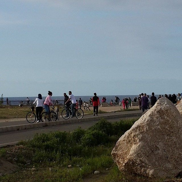 men, large group of people, copy space, lifestyles, clear sky, leisure activity, transportation, person, bicycle, sky, mixed age range, walking, sunlight, land vehicle, mode of transport, medium group of people, tourist, outdoors, travel