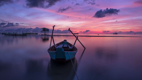 Fishing boat moored in lake against sky during sunset