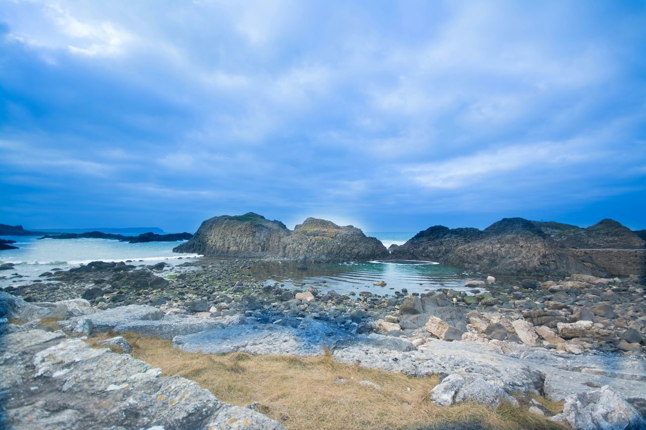 sky, water, scenics, tranquil scene, tranquility, beauty in nature, sea, cloud - sky, nature, mountain, rock - object, cloud, blue, cloudy, rock formation, idyllic, rock, non-urban scene, shore, remote