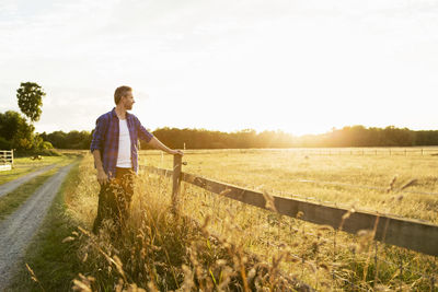 Farmer standing by fence on grassy field during sunny day