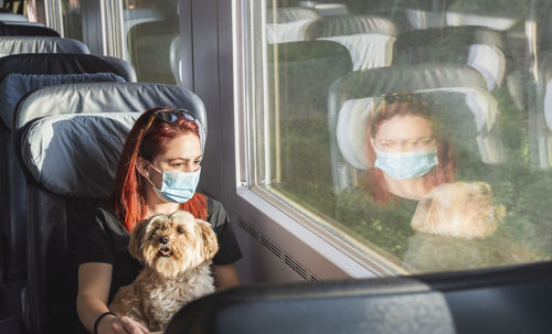 Young woman wearing mask sitting with dog in train