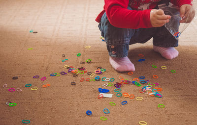 Low section of child putting rubber bands in plastic bag while crouching on carpet at home