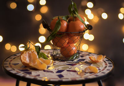 Tangerines in a mesh bucket on a table against a background of bright bokeh