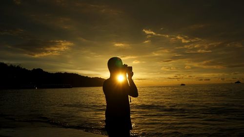 Silhouette hand against sea during sunset