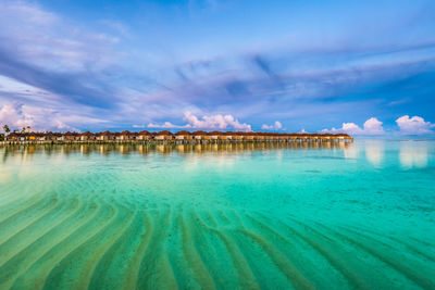 Scenic view of water villas in maldives after sunset with turquoise clear water and dramatic sky