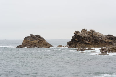 Rock formation in sea against clear sky