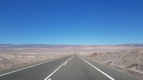 Empty road by desert against clear blue sky