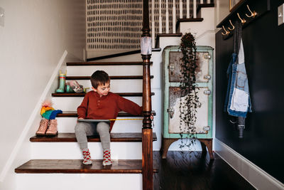 Young boy sitting in stair way using tablet and measuring tape