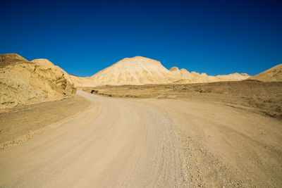 Scenic view of desert road against clear blue sky