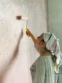 Side view of woman painting wall at home