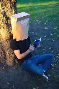 High angle view of man wearing paper bag while reading book outdoors