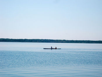 People sitting in boat on sea against clear sky