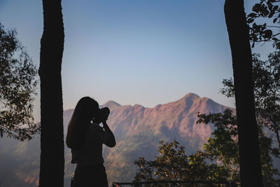 Silhouette man photographing by tree against sky