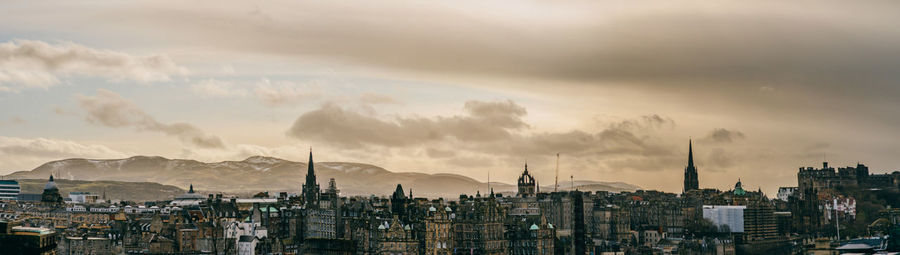 Panoramic view of buildings against cloudy sky and hills