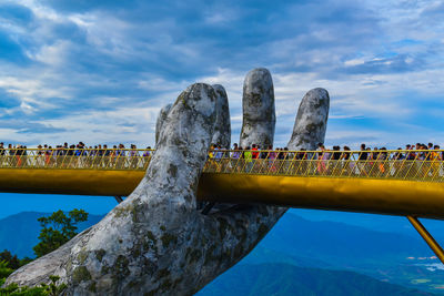Group of people on bridge against cloudy sky