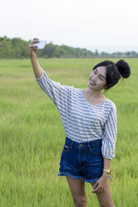 Young woman taking selfie while standing on grassy field