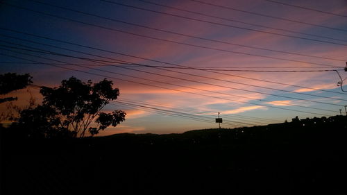 Low angle view of silhouette electricity pylon against sky at sunset