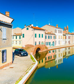 Buildings by river against clear blue sky