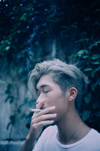 Portrait of young man smoking while looking away outdoors