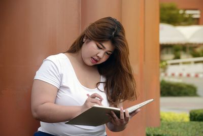 Young woman writing on book by columns 
