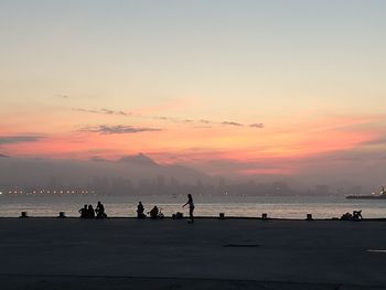 Silhouette people on beach against sky during sunset