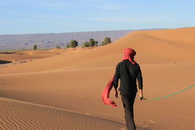 Rear view of woman walking on sand dune in desert