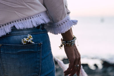 Midsection of woman with flowers in pockets against sky