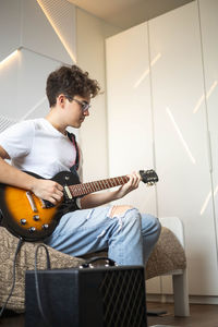 Young man playing guitar while sitting at home