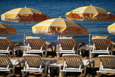 Empty deck chairs by parasols at beach on sunny day