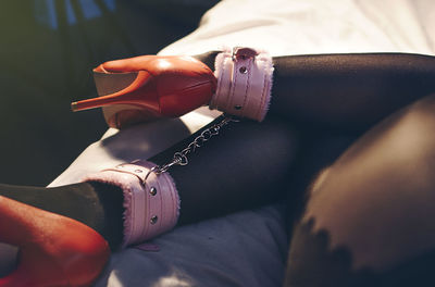 Low section of woman with handcuffs on legs at bed