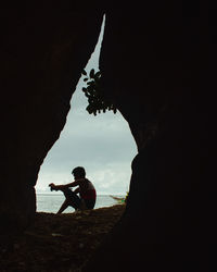 Silhouette man sitting on rock against sky