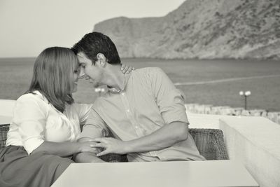 Young romantic couple embracing while sitting on terrace against sea