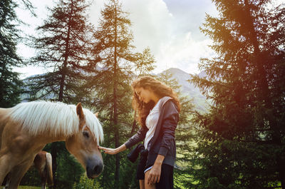 Woman touching horse while standing against trees