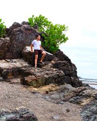 Man standing on rock by sea against sky