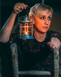Woman looking away while holding lit lantern in darkroom