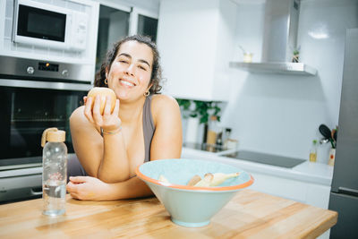 Portrait of young woman eating fruit at home