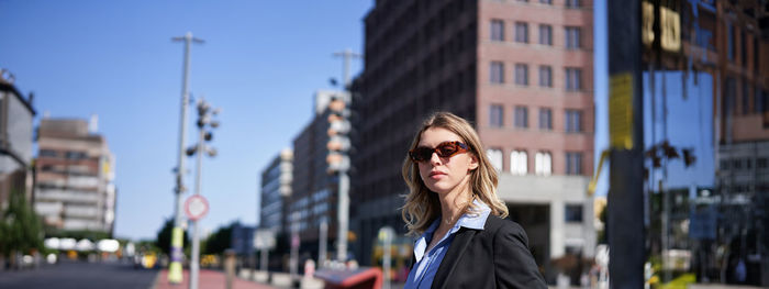 Portrait of young woman standing against buildings