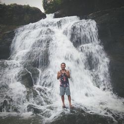 Full length portrait of man standing against waterfall