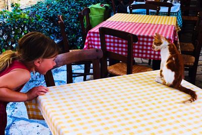 Girl looking away at cat sitting on table