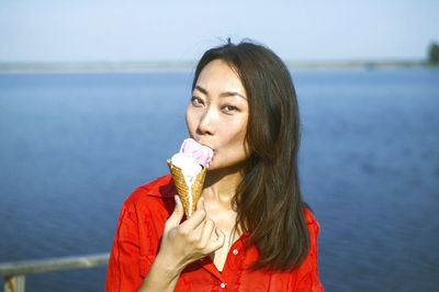 Portrait of woman holding ice cream against sea