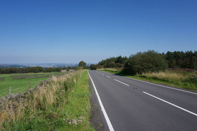 Empty road along landscape and trees against clear blue sky