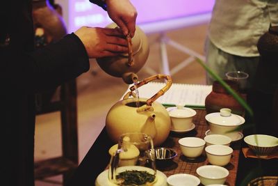 Midsection of person pouring water in teapot on table