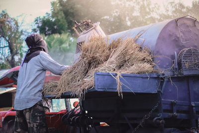 Rear view of farmer collecting hay in agriculture vehicle 