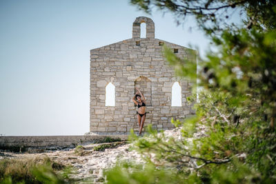 Young woman standing in bikini against stone wall