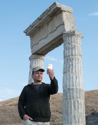 A man takes pictures of himself on his phone against the background of ancient ruins person