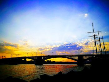 Silhouette bridge over river against sky during sunset