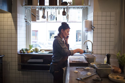 Side view of mature chef talking on mobile phone while preparing food in restaurant kitchen