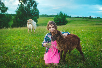 Smiling girl feeding grass to sheep